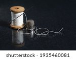 Spool of white thread with needle and thimble