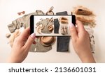 Small photo of Woman taking photo of man’s casual clothes (jeans, khaki shirt) with smartphone. Blogger, influencer or stylist capturing fashion outfit and accessories for social media.