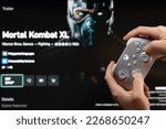 Small photo of New york, USA - February 20, 2023: Buy new game Mortal Kombat XL in online microsoft xbox store with gamepad controller in hand