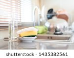 Yellow sponges and dish washing liquid soap on dirty sink fully with dishes and kitchen ware.