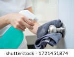 Woman house keeper cleaning a dirty stainless door knob in toilet. Maid spraying liquid cleaning solution on the dirty door knob handle in toilet and using micro fabric wipe on door knob surface.
