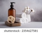 Brown dispenser bottle, loofah sponge and white towels. Set of bathroom accessories. 