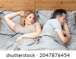 Small photo of Two in bed, a woman looks with suspicion at a man who has turned away in the other direction. Relationship concept