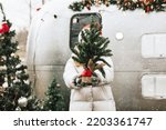 teenage girl in Santa hat stands with Christmas tree on Christmas morning and celebrate New Year or Christmas outdoor near trailer mobile home recreational vehicle, local travel