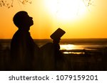 silhouette of young man turns to God with questions about life sitting under tree on the lawn, male on the nature looking up at the sky with fatigue and the hope, the concept of faith and spirituality