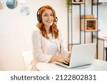Young beautiful redhead customer service operator woman with headphones working from home. Internet communication, customer support, online meeting concept