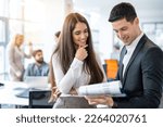 Small photo of Attractive young woman in formal wear checking financial reports and paperwork with handsome good looking man in suit while standing in office.