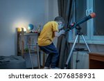Small photo of Cute boy is looking through a telescope in a room at the night starry sky. Children's scientific hobbies and space exploration