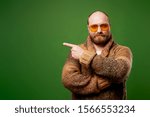 Small photo of Bald man in sweater pointing his hand to empty place against green background