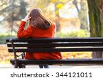 Back view of lonely young brunette woman sitting on a bench in the park