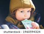 Close up portrait of sweet toddler kid eating fruit puree from plastic doy pack, sitting in stroller, outdoor snack time