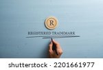 Small photo of Letter R cut into wooden cut circle and male hand writing a Registered trademark sign under it. Over pastel blue wooden background.