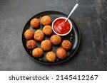 Small photo of Fried potato cheese balls in tomato sauce, croquettes cottage cheese Paneer ball meat balls on black plate over dark background. fast food, top view