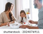 Young family has lunch at table in bright kitchen at home. The daughter does not want to eat and parents are worried
