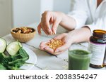 Woman doctor nutritionist hands in white shirt with omega 3, vitamin D capsules with green vegan food. The doctor prescribes a prescription for medicines and vitamins at the clinic