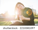 Portrait of young happy woman with long hair with paper cup of coffee in city park on golden hour
