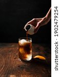 Small photo of Preparing espresso tonic with orange juice. A hand pouring espresso from a small white can into a highball glass filled with ice spheres and tonic.