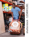 Small photo of Focused African American diligent cheerful smiling carrying handbarrow with construction supplies purchased in shop of building materials