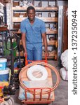 Small photo of Focused African American diligent positive cheerful smiling carrying handbarrow with construction supplies purchased in shop of building materials