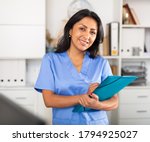 Small photo of Polite latina female health worker meeting patient in medical office, filling out medical form at clipboard