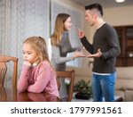 Portrait of unhappy preteen girl sitting at home while parents quarreling