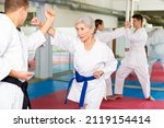 Small photo of Sporty determined elderly woman in kimono practicing martial arts techniques paired with experienced trainer in training room