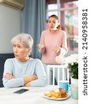Small photo of Portrait of offended aged mother sitting at home table, listening to reproaches from her adult daughter .