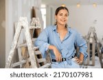 Portrait of young woman standing at stepladder in apartment during repair works.