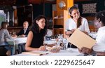 Small photo of positive female busboy taking order to couple in modern restaurante