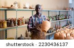 Small photo of Professional confident African American potter proffering goods in pottery shop