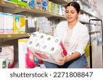 Young woman looking to buy pack of toilet paper in supermarket