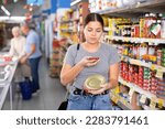 Female customer scanning barcode on aluminum canned food with smartphone while shopping in supermarket, paying for item using mobile app