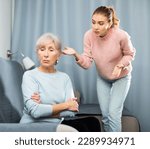 Small photo of Portrait of offended elderly mother sitting on sofa at home, listening to reproaches from disgruntled adult daughter .