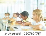 Small photo of Focused cute towheaded preteen schoolgirl writing exercises in workbook in classroom during lesson