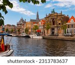 Small photo of HAARLEM, NETHERLANDS - AUGUST 08, 2022: View of historic area of Haarlem on banks of Spaarne river overlooking Teylers Museum and tall belfry of Protestant church Grote Sint-Bavokerk on sunny day ..