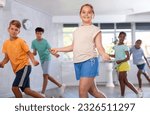 Small photo of Girlie performs movements during warm-up, limbering-up part of workout together with peers. Group of young girls and guys dance modern waacking in fitness club unfocused