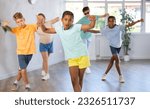 Small photo of African girlie performs movements during warm-up, limbering-up part of workout together with peers. Group of young girls and guys dance modern hip hop in fitness club unfocused