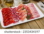 Small photo of Slices of Spanish dry-cured gammon, variety of sausages and bacon served with greens and olives on rectangular plate
