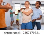 Small photo of African boy and European girlie learn figures of pair dance and train before competition. Children fitness group is engaged in studio