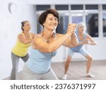 Small photo of Three senior women in gym are teaching dance moves of modern trends. Active longevity, healthy generation, hobbies
