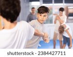 Small photo of Diligent preteen student practicing self-defense techniques in pairs during workout session
