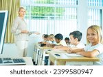 Small photo of Portrait of cheerful towheaded preteen schoolgirl sitting at desk in classroom during lesson