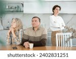 Small photo of Livid middle-aged man sitting at the kitchen-table next to old female family member looking upset