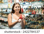 Small photo of Rapt young woman choosing Spanish dancer statuette among various souvenirs in gift shop in Barcelona
