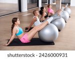 Four people doing v-sits exercises on swiss ball during pilates training