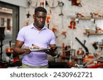 Small photo of African-american man reading price catalogue while standing in salesroom of gardening tools store.