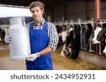 Small photo of Skilled middle-aged male farmer carrying milk churn near stall with cows during work on dairy farm