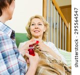 Small photo of woman visiting sick friend and giving her a linctus at home