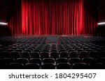 Darkened empty movie theatre and stage with the red curtains drawn viewed over rows of vacant seats from the rear