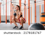 Small photo of Determined female athlete looking away and doing goblet squat with heavy kettlebell during intense training in spacious light gym